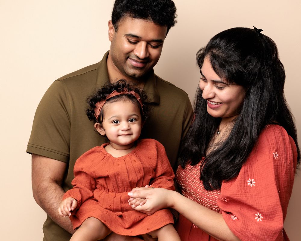 A loving family portrait of three wearing warm earth tones against a neutral background.