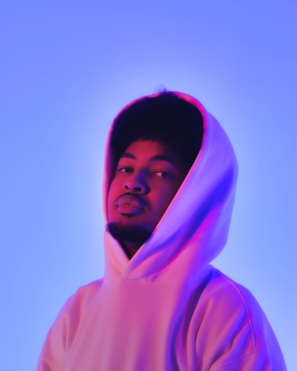 Atmospheric portrait with neon pink and blue lighting of person wearing white hoodie.