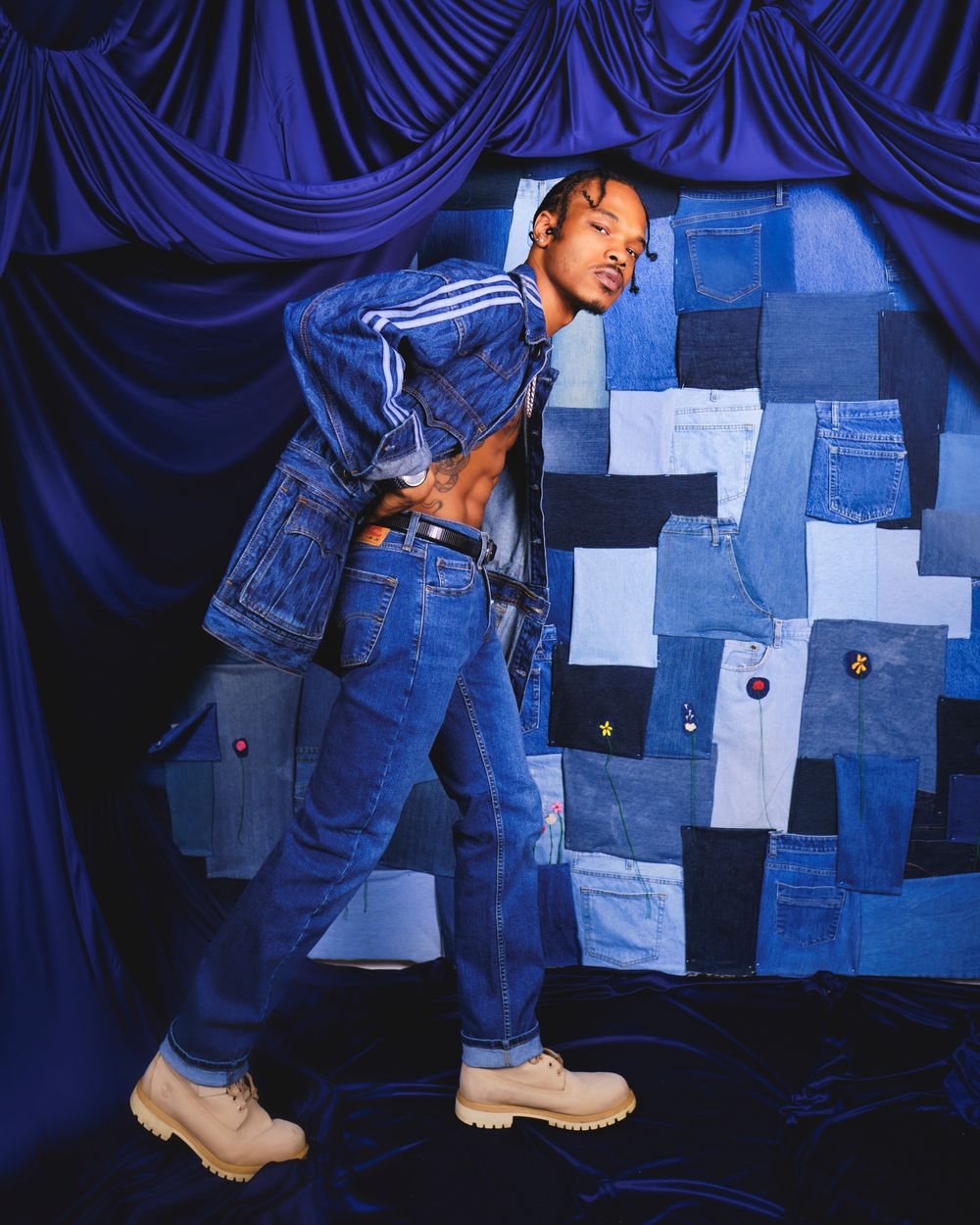 Fashion portrait against blue draped backdrop with denim patchwork wall.