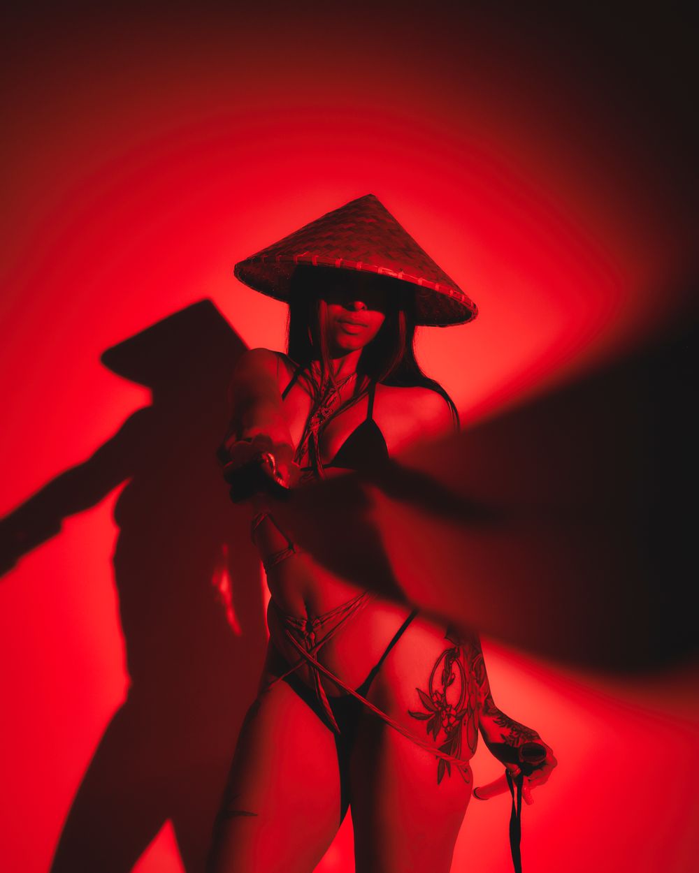 Dramatic red-lit silhouette wearing Asian conical hat in artistic pose.