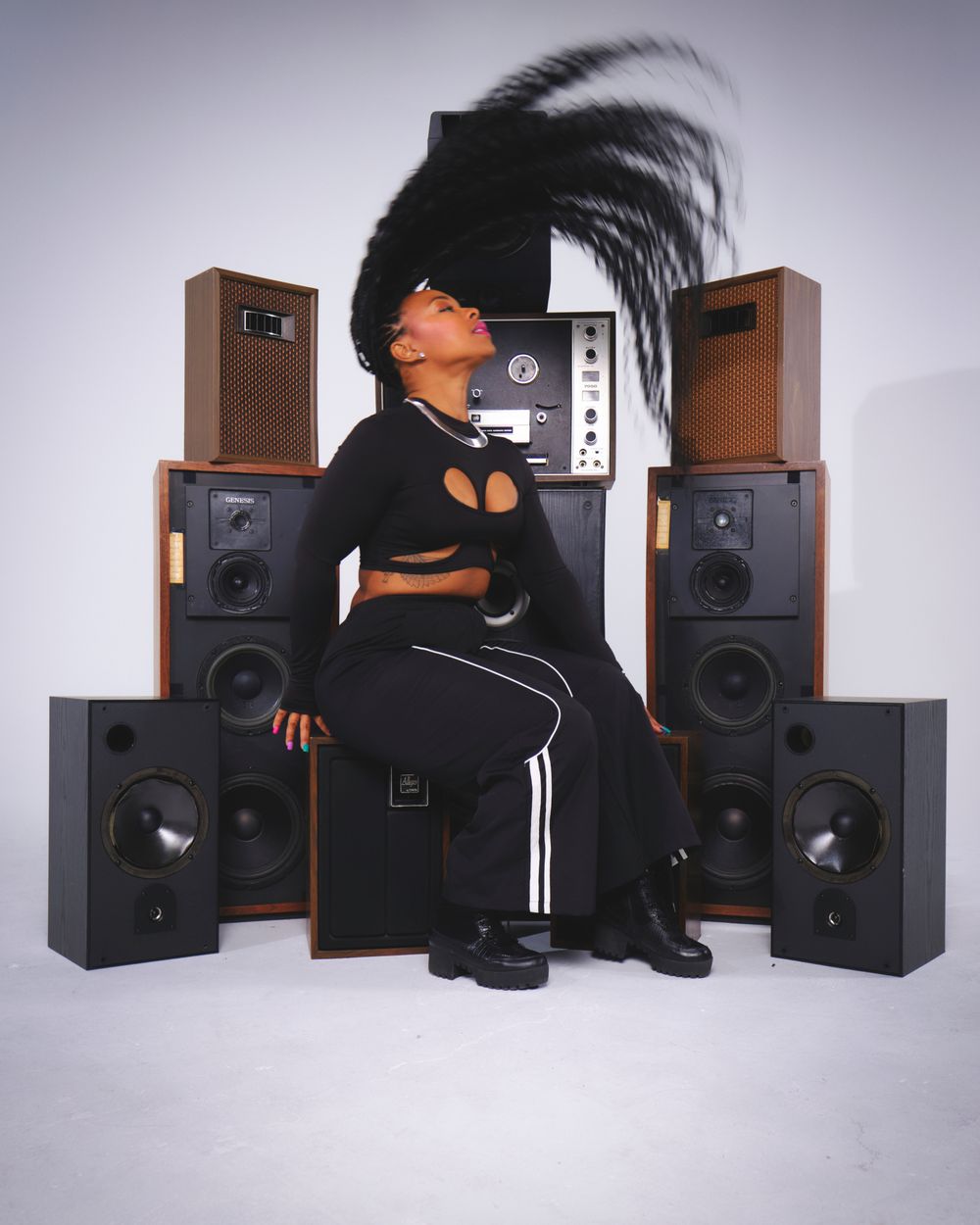 Stylish portrait with tall speakers and dramatic hair movement against studio backdrop.