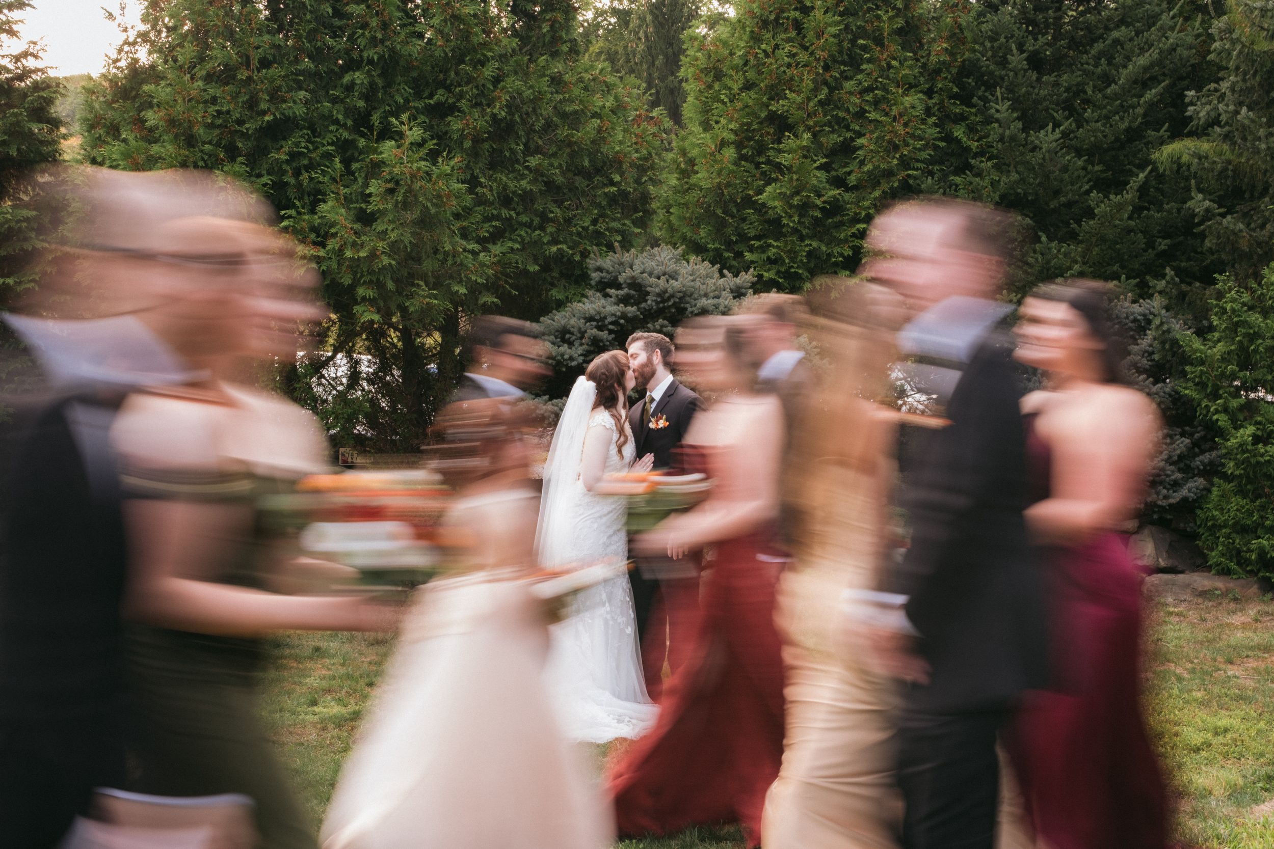 Motion blur photograph of wedding party dancing and celebrating outdoors surrounded by evergreen trees.