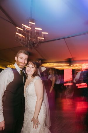 Couple poses on a dance floor at wedding reception with moody lighting and chandelier overhead.