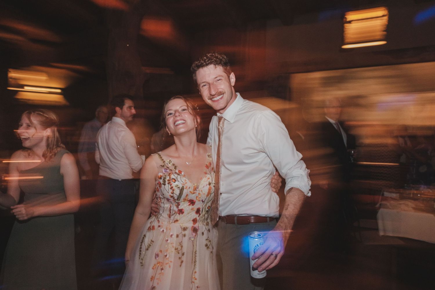 A couple dances at a celebration in a dark room with motion blur and warm lighting effects.