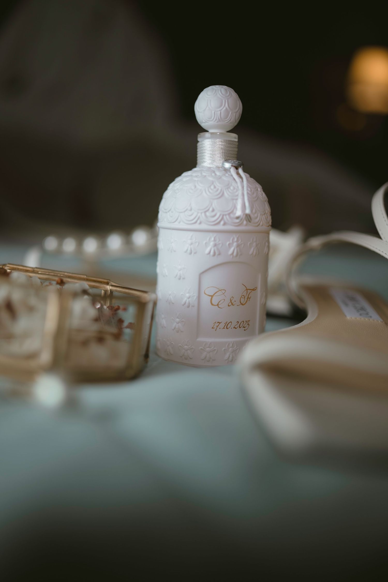 Elegant white perfume bottle with ornate design sitting on table with wedding accessories.