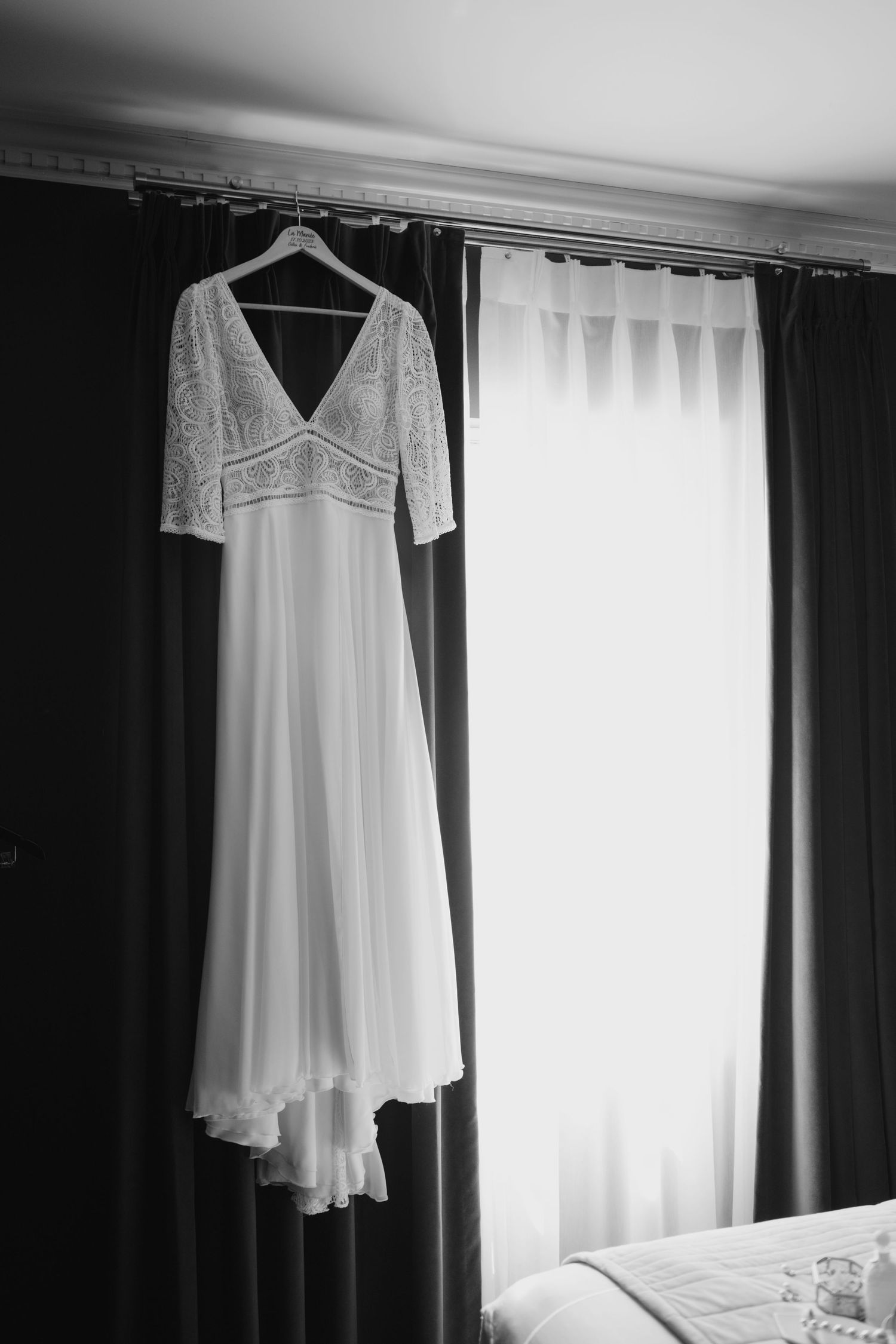 Vintage-style white wedding dress hanging by window in black and white photography.