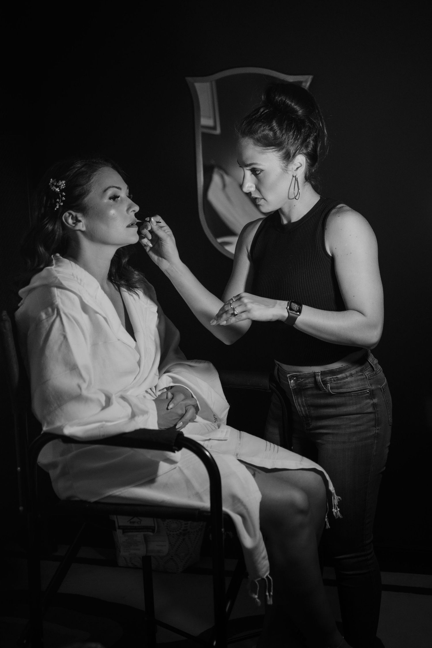 Black and white image of makeup artist applying cosmetics during wedding preparation.