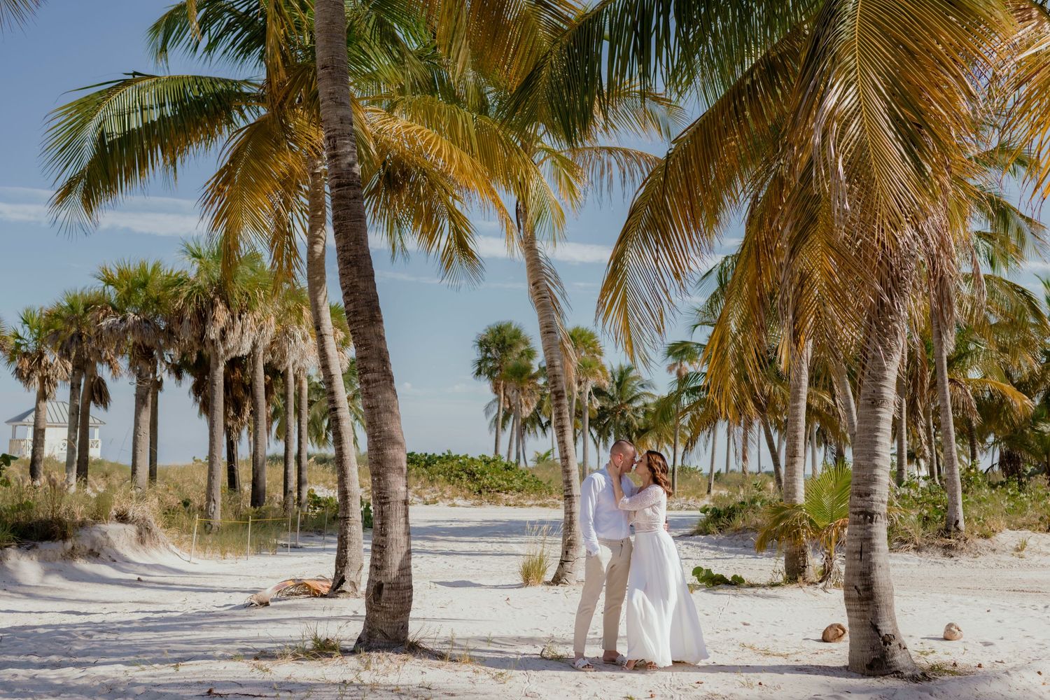 Beach wedding scene with palm trees and couple on white sand.