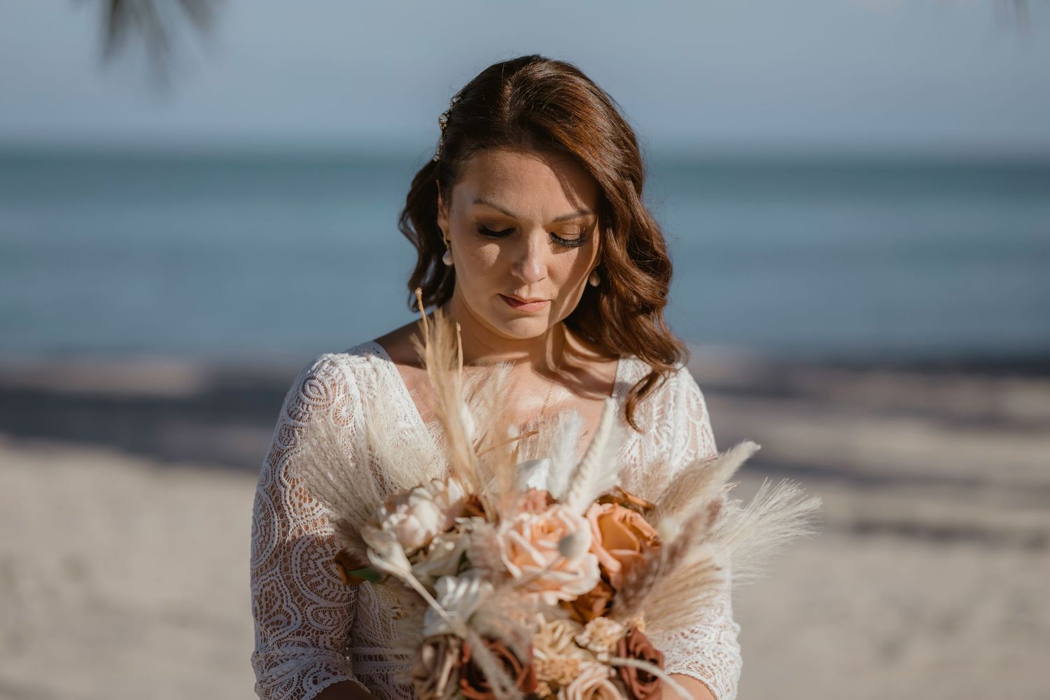 Bride holding dried flower bouquet on tropical beach.