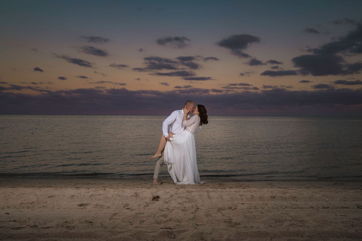 A dramatic sunset beach wedding photo showing a couple in an intimate pose against the darkening sky.