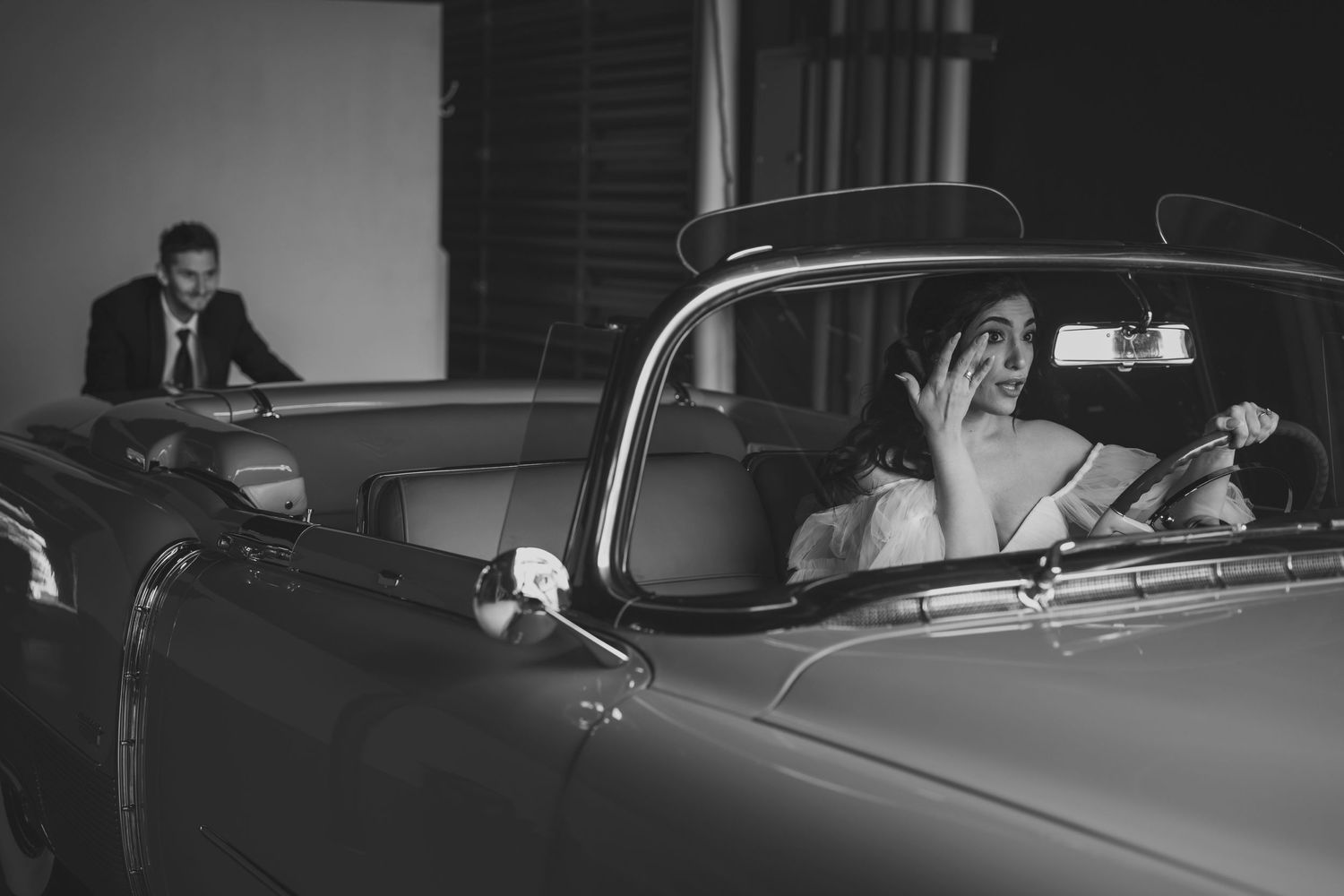 Classic black and white photo of newlyweds in vintage car setting.