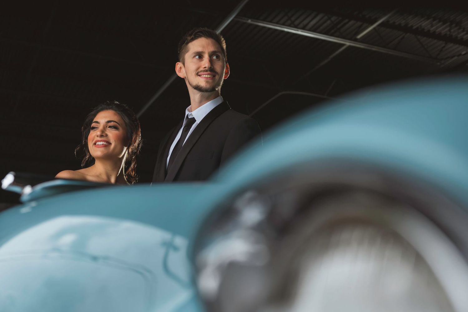 A dramatic low angle shot of a couple with a vintage blue Cadillac in the foreground.