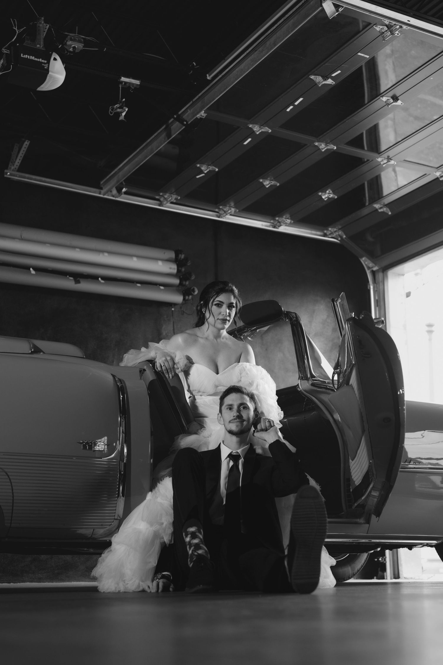 A playful black and white wedding photo with a couple posing in an industrial garage setting.