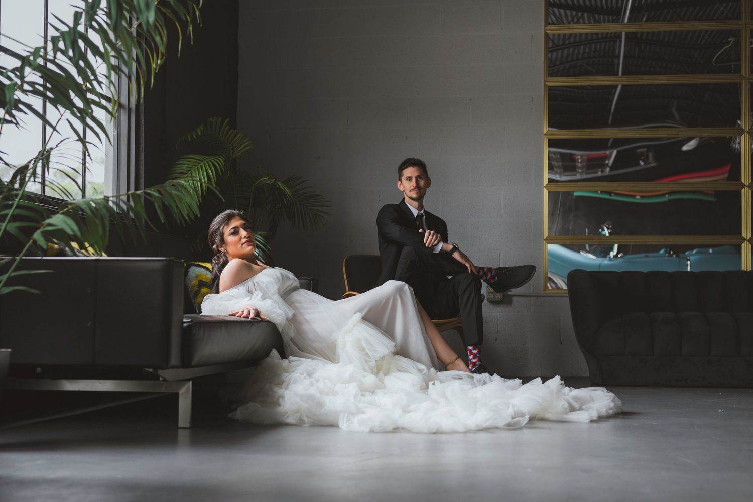 Modern wedding portrait with couple lounging dramatically in an industrial space with plants.