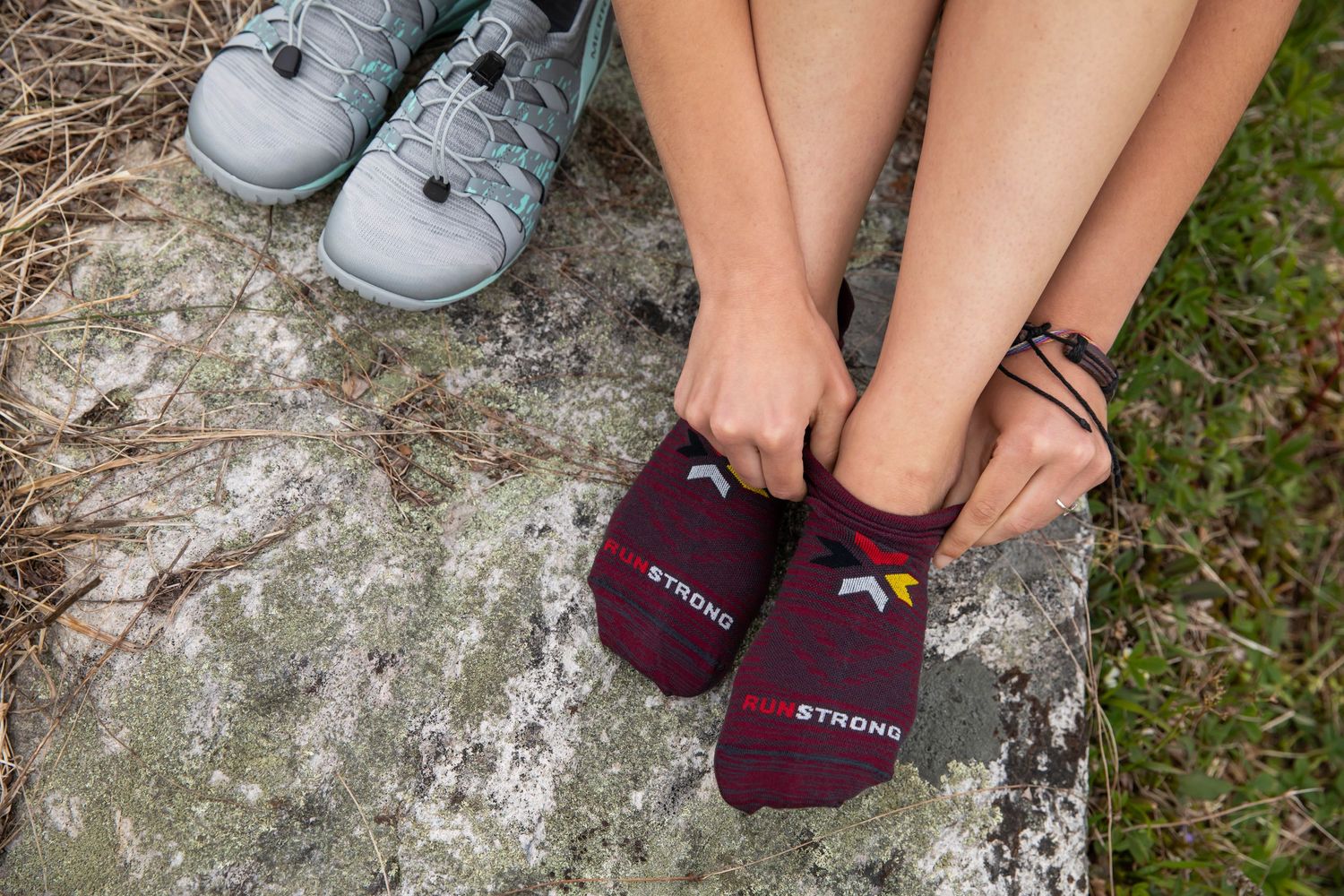 Photo of a woman sitting on a rock in the forest, putting on Run Strong socks from Fox River Mills before going for a run