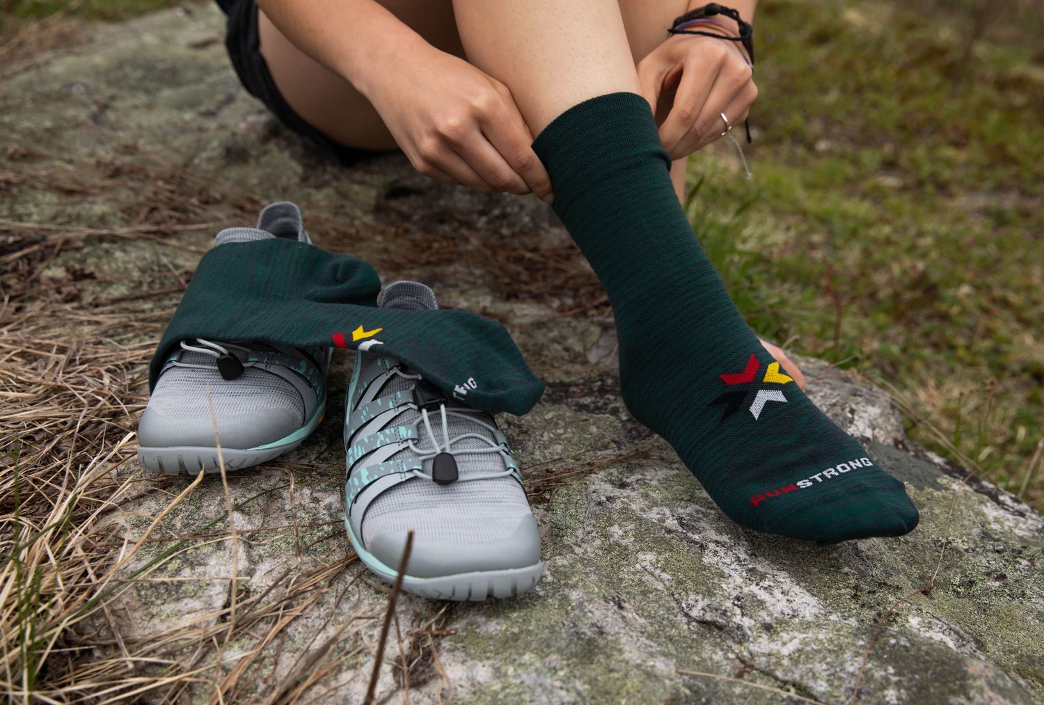 Photo of a woman sitting on a rock in the forest, putting on Run Strong socks from Fox River Mills before going for a run