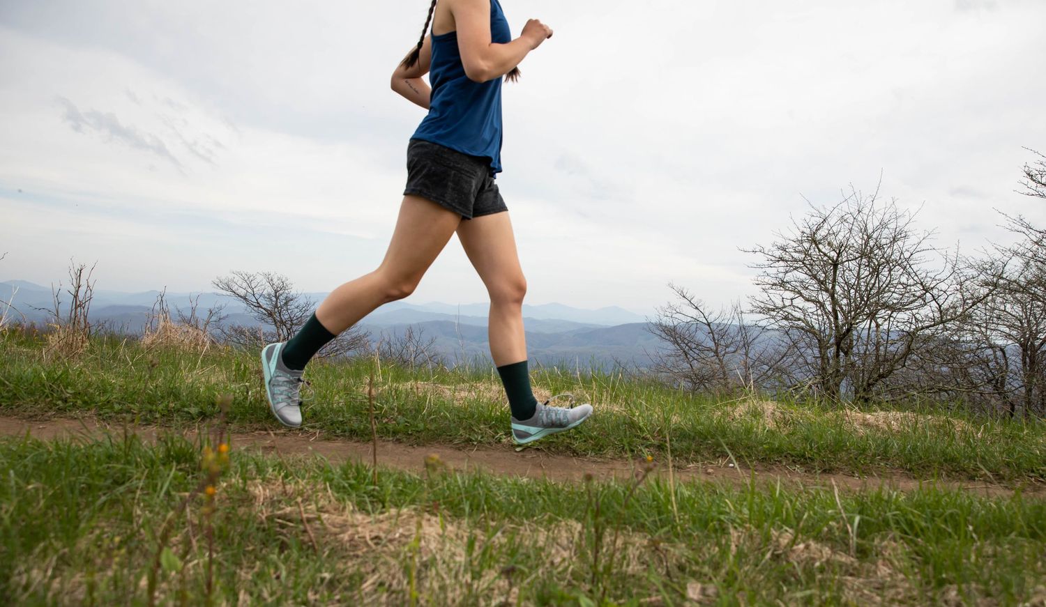 Photo of a woman running on a trail on a mountainside wearing Run Strong socks, Whitetop Mountain, Virginia