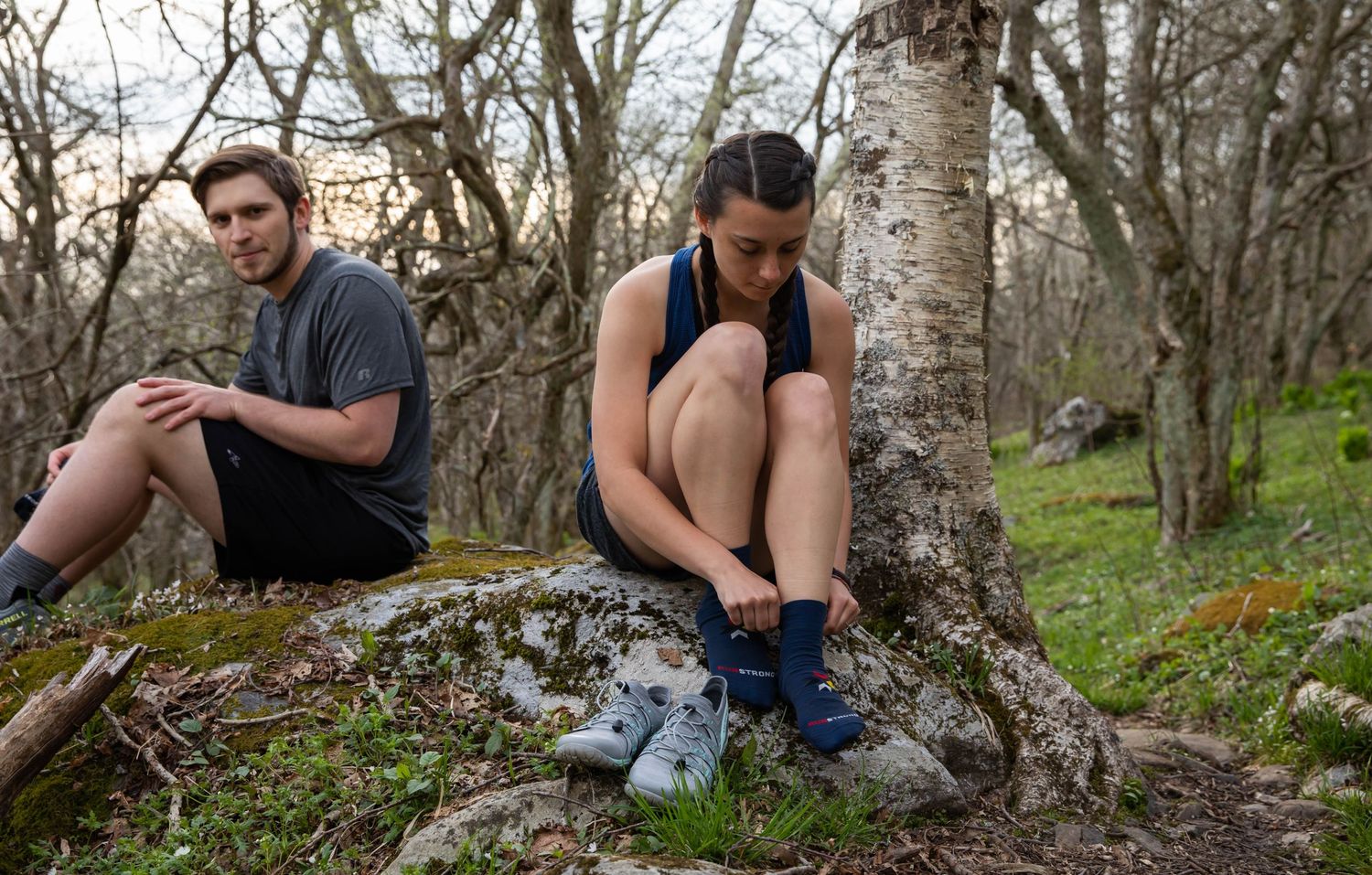 Photo of a couple sitting on a rock beside a trail, putting on socks and running shoes before going for a run