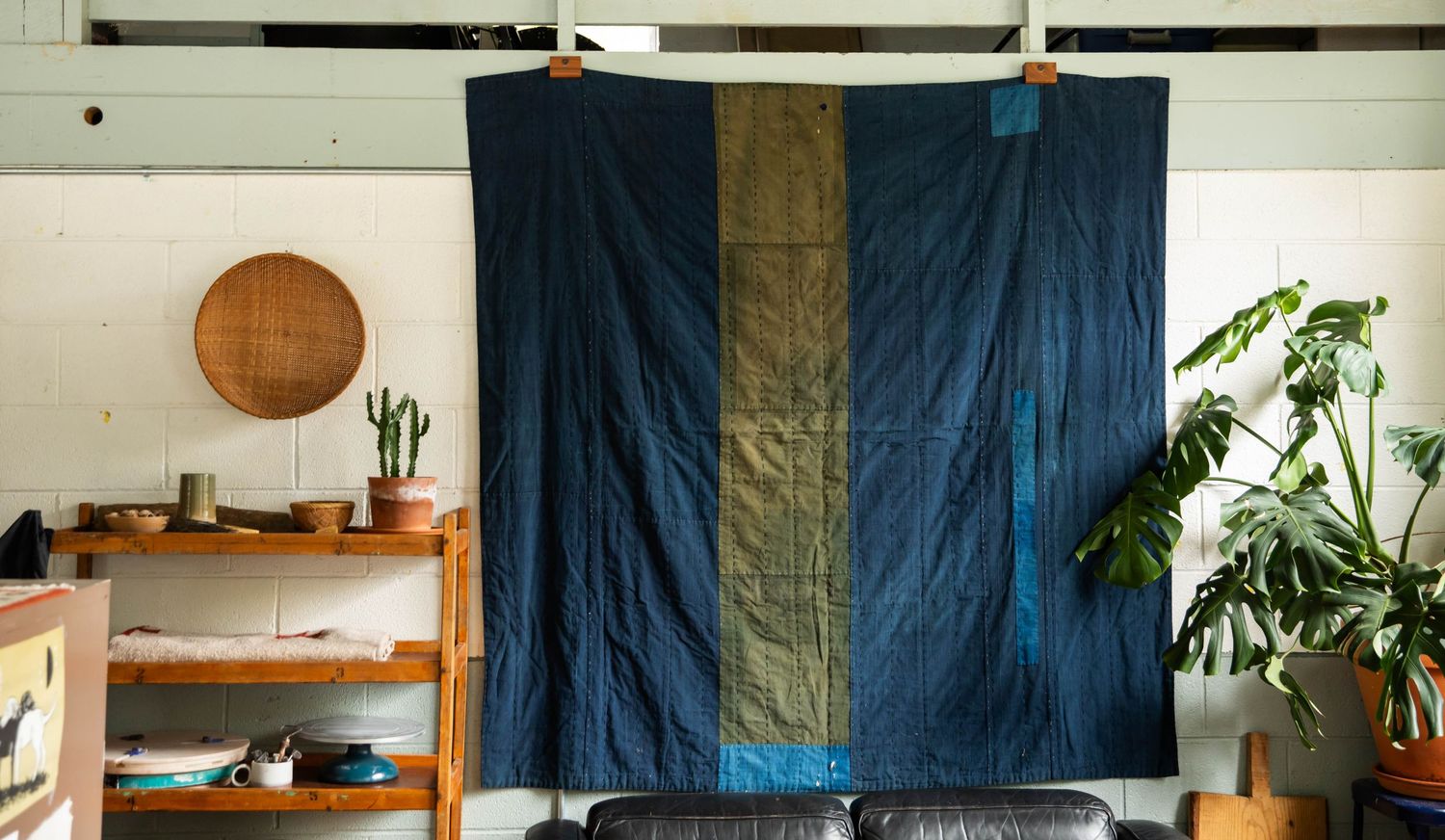Portrait of a large blue and green antique quilt hanging in a pottery studio in Boone, NC