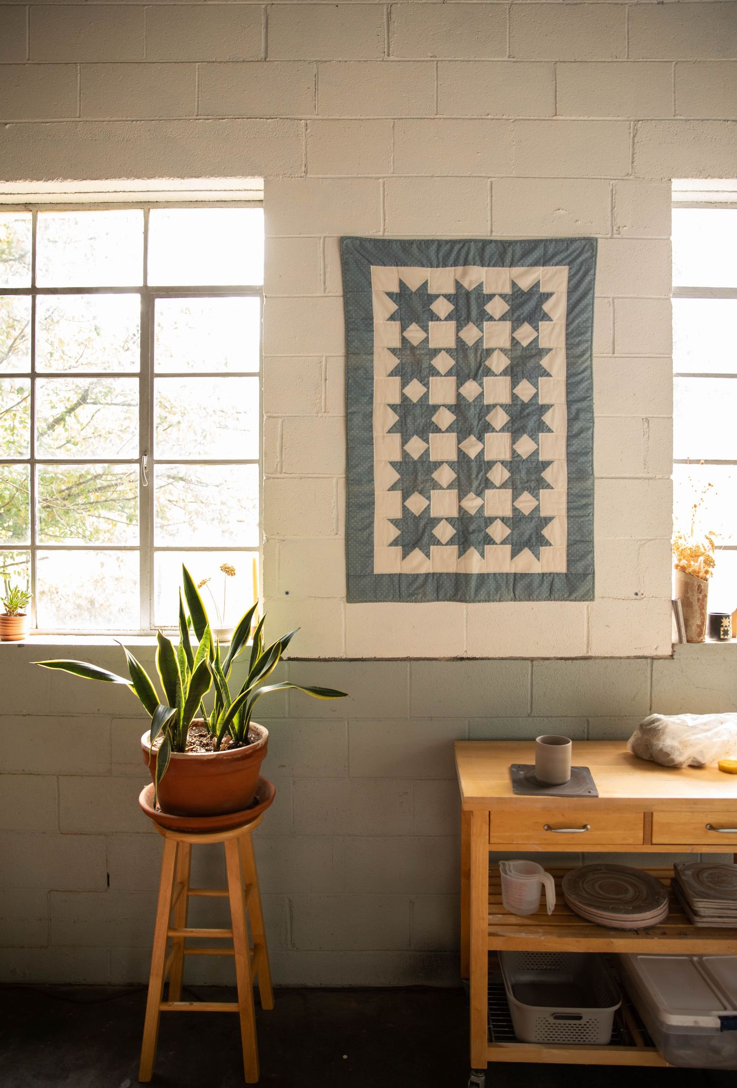 Photo of quilt hanging in a pottery studio with window light and plants