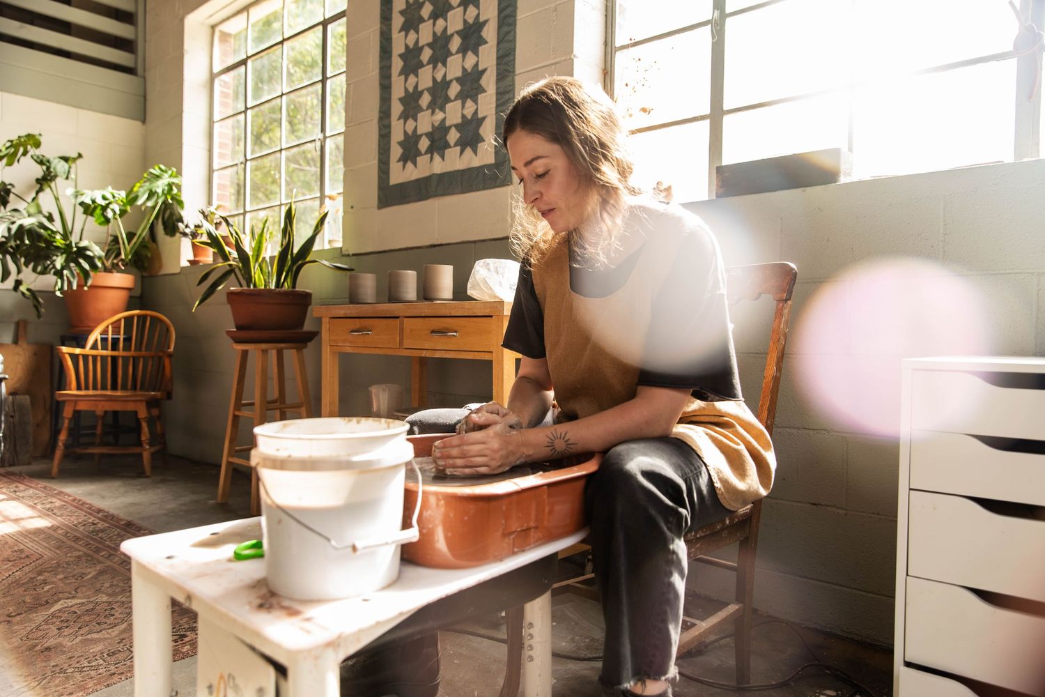 Photo of a potter at work at her wheel by the window with beautiful light