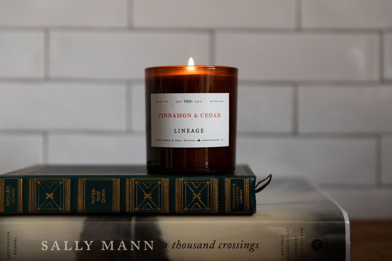 Photo of a Lineage brand candle on a stack of books in front of a white subway tile backsplash