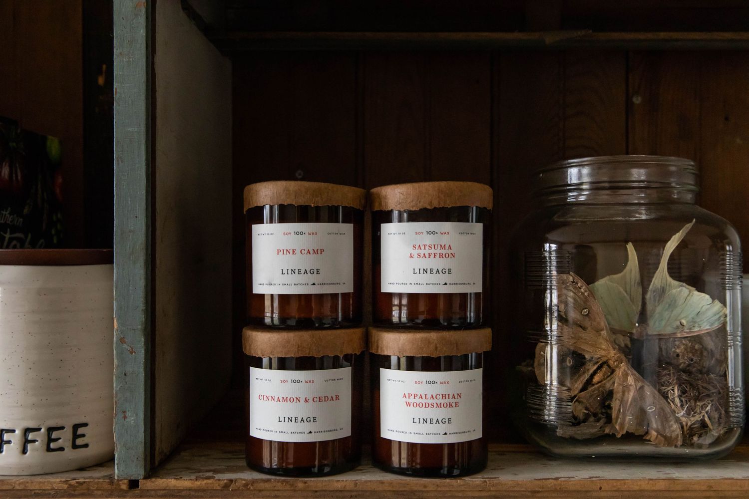 Photo of Lineage brand candles on a shelf with a glass jar full of nature inspired collectibles