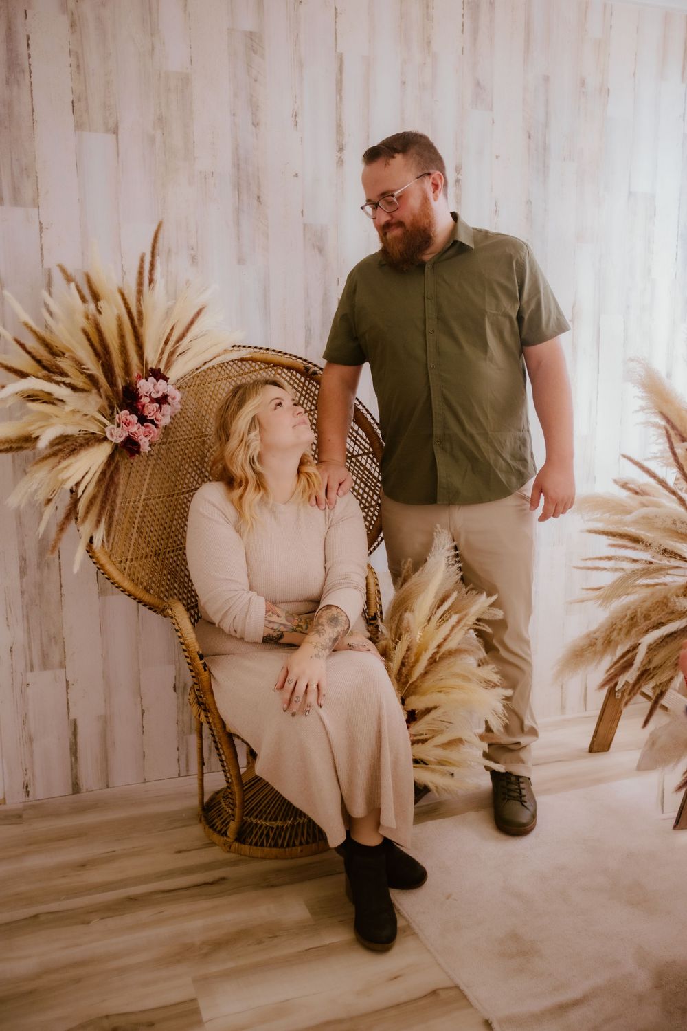 Romantic photo session featuring a couple in casual attire posing against a neutral backdrop with dried palm leaves.