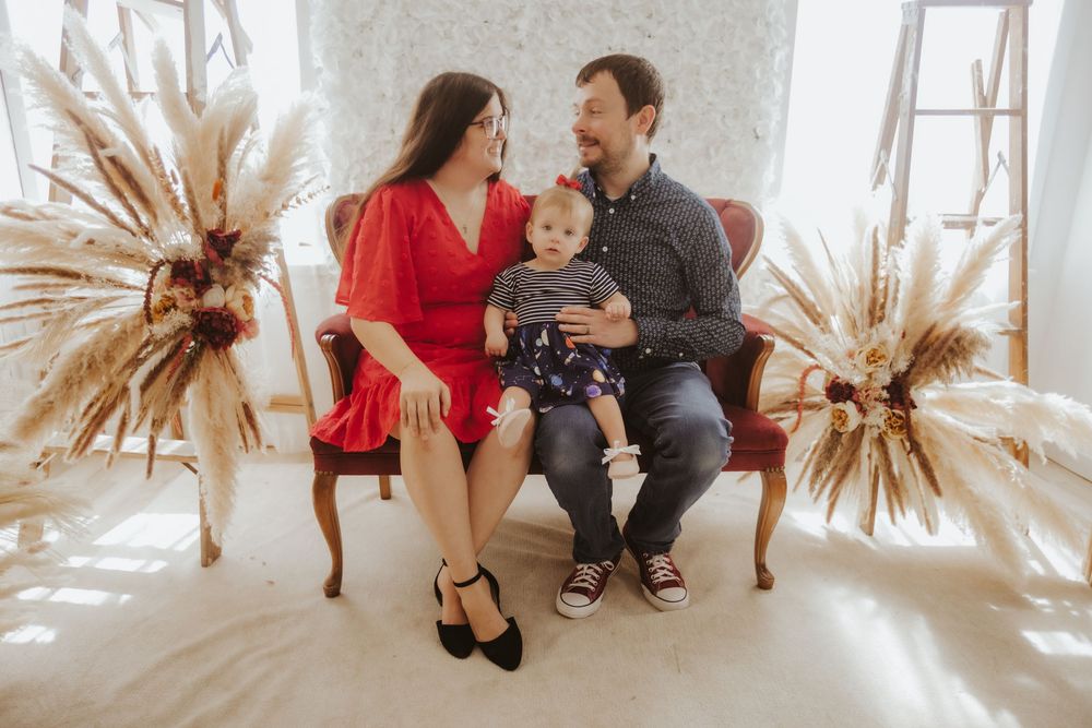 A family sits together in a bright room with a decorative dried palm leaf sunburst on the wall.