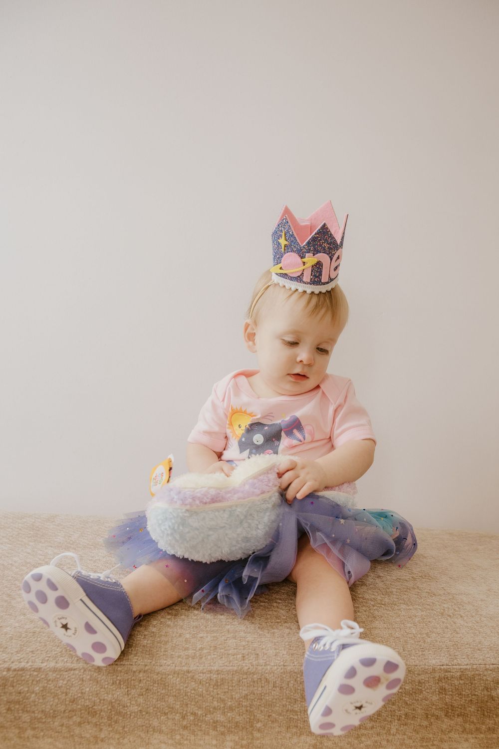 Baby wearing pink outfit and crown sits on beige carpet in series of connected milestone photos.