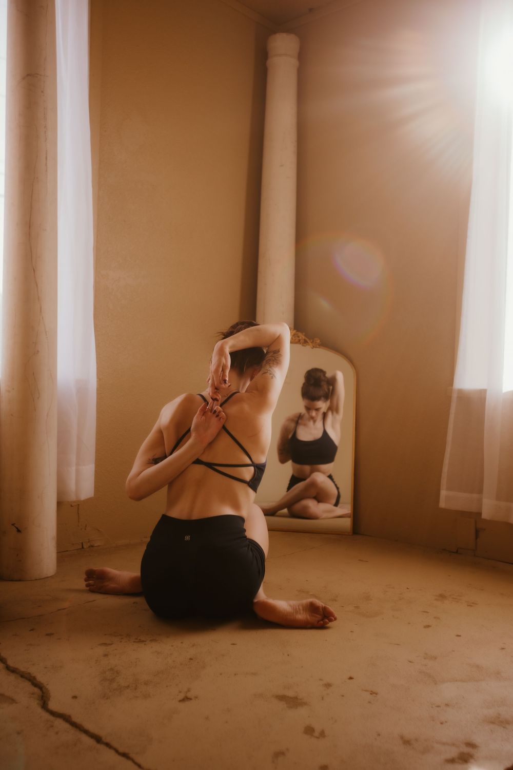 Multiple people practice yoga poses on a concrete floor in a dimly lit room with white columns.