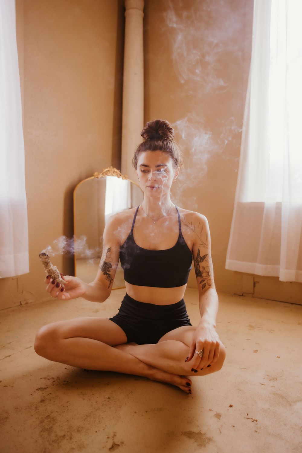 A series of artistic photos showing a person in black athletic wear sitting on the floor with smoke effects in warm lighting.