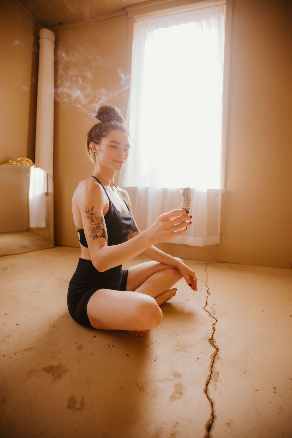 A person in black attire sits on a bare floor near a window, creating a series of artistic contemplative poses.