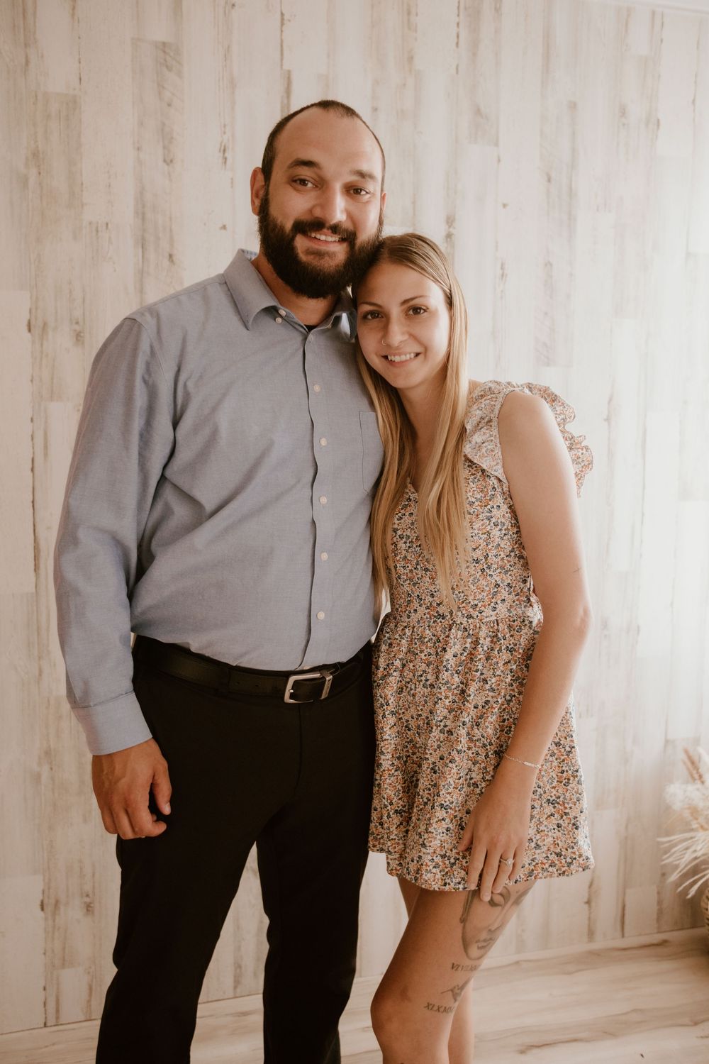 A couple poses together against a light wooden wall in a romantic photoshoot series.
