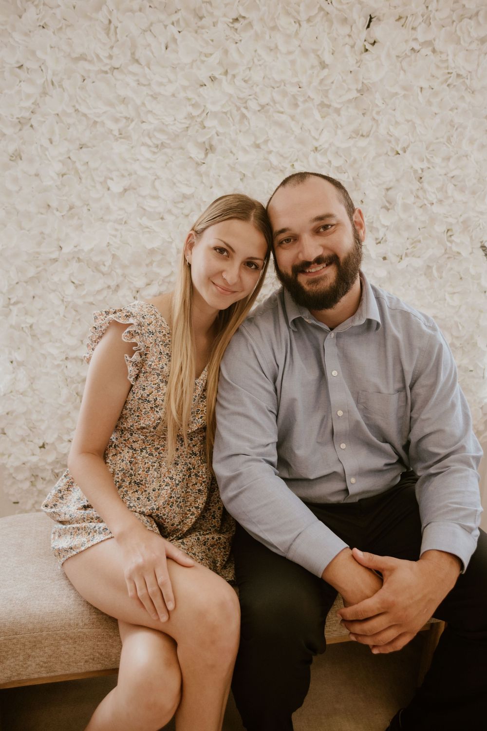A couple sits close together against a textured wall in a series of intimate engagement-style photos.