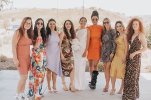 Wedding party in colorful dresses poses together outdoors on sunny day.