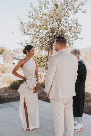 An outdoor wedding ceremony with a couple in matching white attire standing before blooming trees.