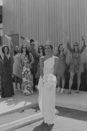 Black and white photo of wedding party celebrating with raised arms behind bride.