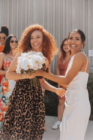 Two women sharing a joyful moment with white orchids at a celebration.