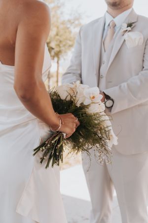 A close-up of wedding attire details showing white formal wear and an elegant orchid bouquet.