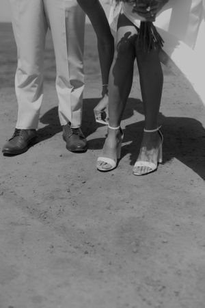 A black and white close-up of wedding shoes and formal attire.