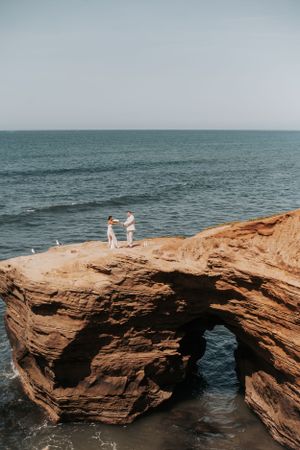 Two figures standing on a dramatic rocky ocean cliff formation.