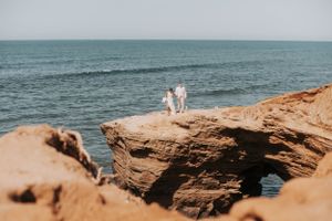 A distant view of a coastal wedding ceremony on rugged rock formations.