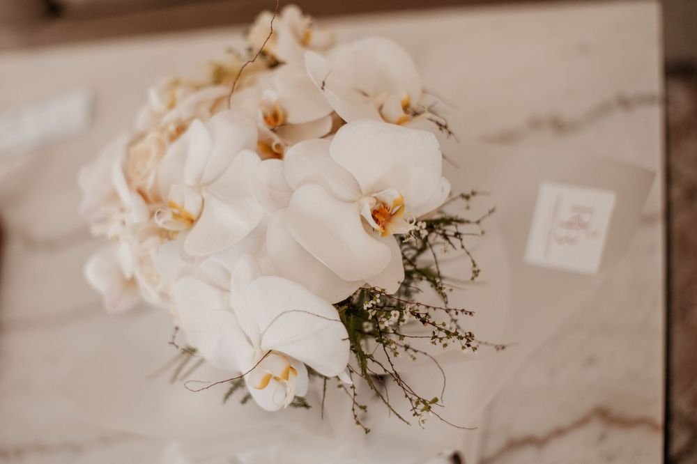 An elegant white orchid wedding bouquet with delicate greenery against a marble surface.