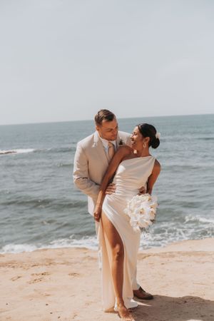 Romantic beachside wedding portrait with waves crashing in background.