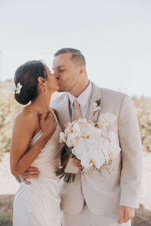 A romantic wedding moment captured as couple embraces with white orchid bouquet in hand.