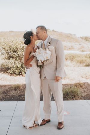Newlyweds in matching cream-colored attire share an intimate moment against a scenic backdrop.