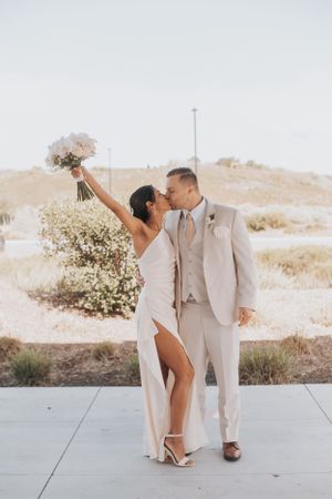 A celebratory moment as couple poses with raised bouquet against desert landscape.