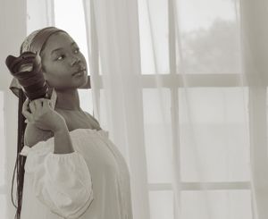 Elegant profile portrait with dramatic lighting by a window, soft white fabric and natural light creating a dreamy atmosphere.