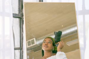 Person in white top against window with green hair accessories looking up thoughtfully in natural light setting.